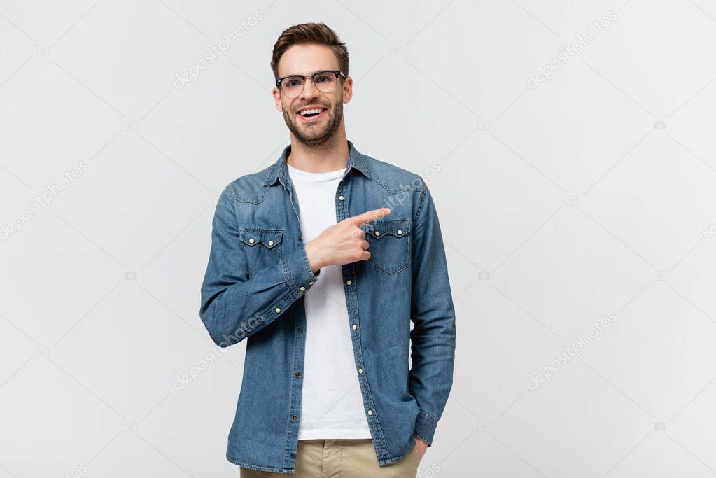Positive man in eyeglasses pointing with finger away isolated on grey