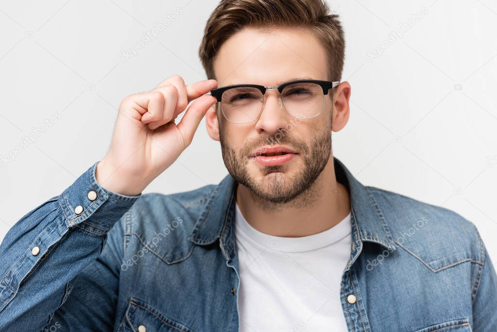 Young man squinting while touching eyeglasses isolated on grey