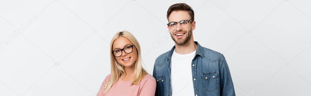 Smiling couple in eyeglasses looking at camera isolated on grey, banner 