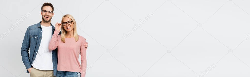 Man in eyeglasses hugging smiling girlfriend isolated on grey, banner 