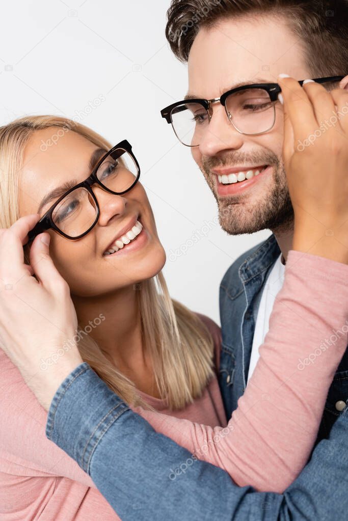 Young couple smiling at each other while touching eyeglasses isolated on grey