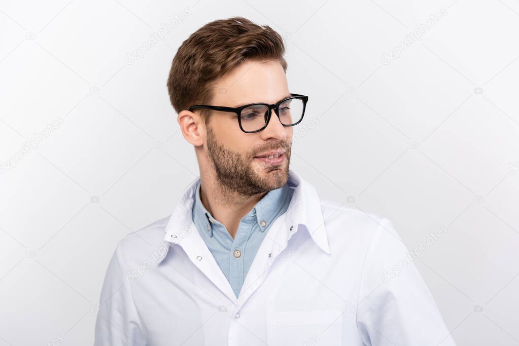 Smiling ophthalmologist in eyeglasses and white coat looking away isolated on grey 