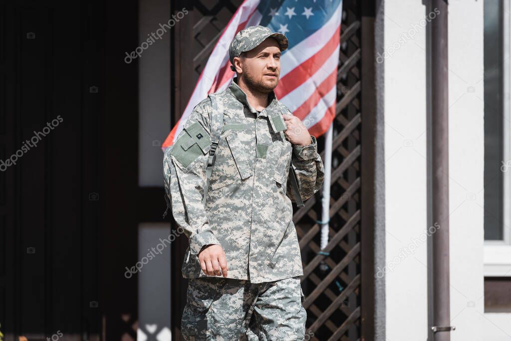 Confident military man looking away while standing near house and american flag