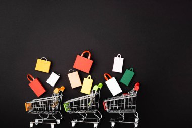 Siyah arka planda renkli alışveriş çantaları olan oyuncak arabaların üst görüntüsü 
