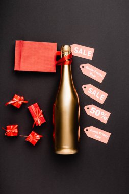 Top view of golden bottle of champagne near price tags and toy gifts on black background  clipart