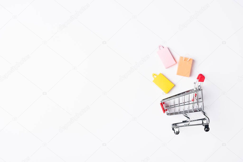 Top view of toy shopping bags near cart on white background