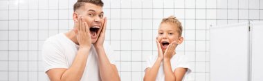Shocked father and son shouting while touching cheeks with hands in bathroom, banner clipart