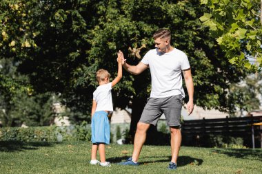 Anaokulu çocuğu ve spor giyim bölümünde genç bir adam parkta birbirlerine beşlik çakıyorlar.