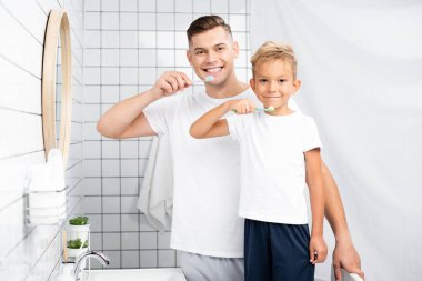 Banyoda lavabonun yanında dikilirken kameraya bakan mutlu baba ve oğul.