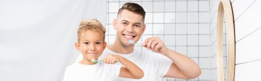Smiling son and father holding toothbrushes and looking at camera, banner clipart