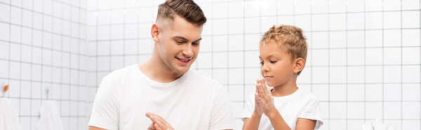 Positive father and son rubbing soap between hands in bathroom, banner