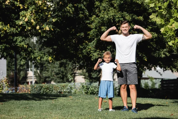 Uśmiechnięty Ojciec Syn Patrząc Kamerę Podniesionymi Rękami Pokazującymi Moc Parku — Zdjęcie stockowe