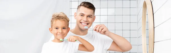 Усміхнений Син Батько Тримають Зубні Щітки Дивляться Камеру Банер — стокове фото