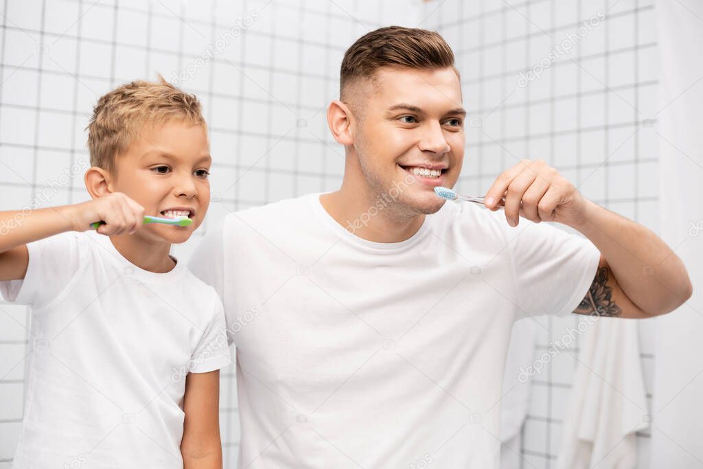 Father and son with toothbrushes showing teeth while looking away in bathroom