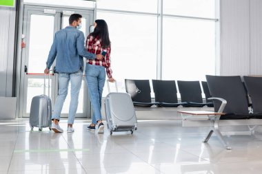 Havaalanında bavullarıyla yürüyen çok kültürlü bir çiftin arka görüntüsü. 