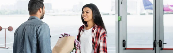 Hombre Sosteniendo Flores Envueltas Mientras Encuentra Sonriente Mujer Afroamericana Aeropuerto — Foto de Stock