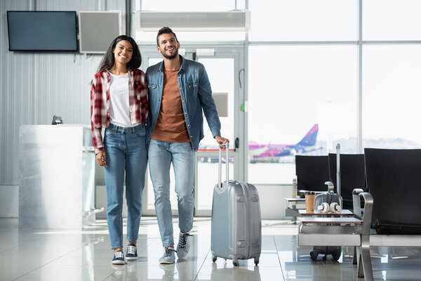 happy multicultural couple with luggage walking in modern airport 