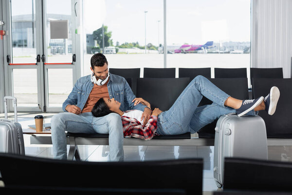 happy african american woman lying near bearded man in departure lounge 