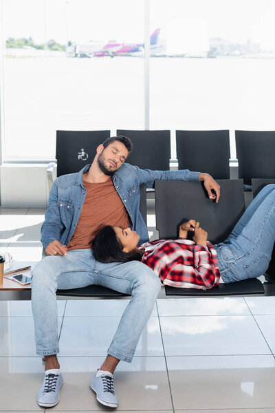 African american woman lying near sleepy man in departure lounge of airport