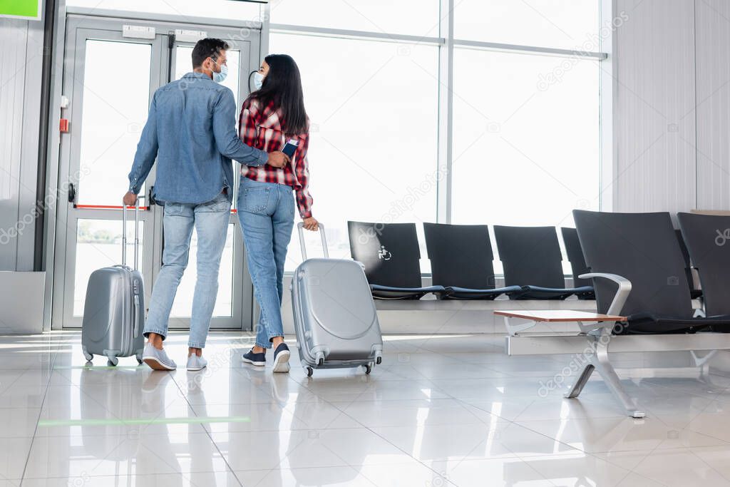back view of multicultural couple walking with luggage in airport 