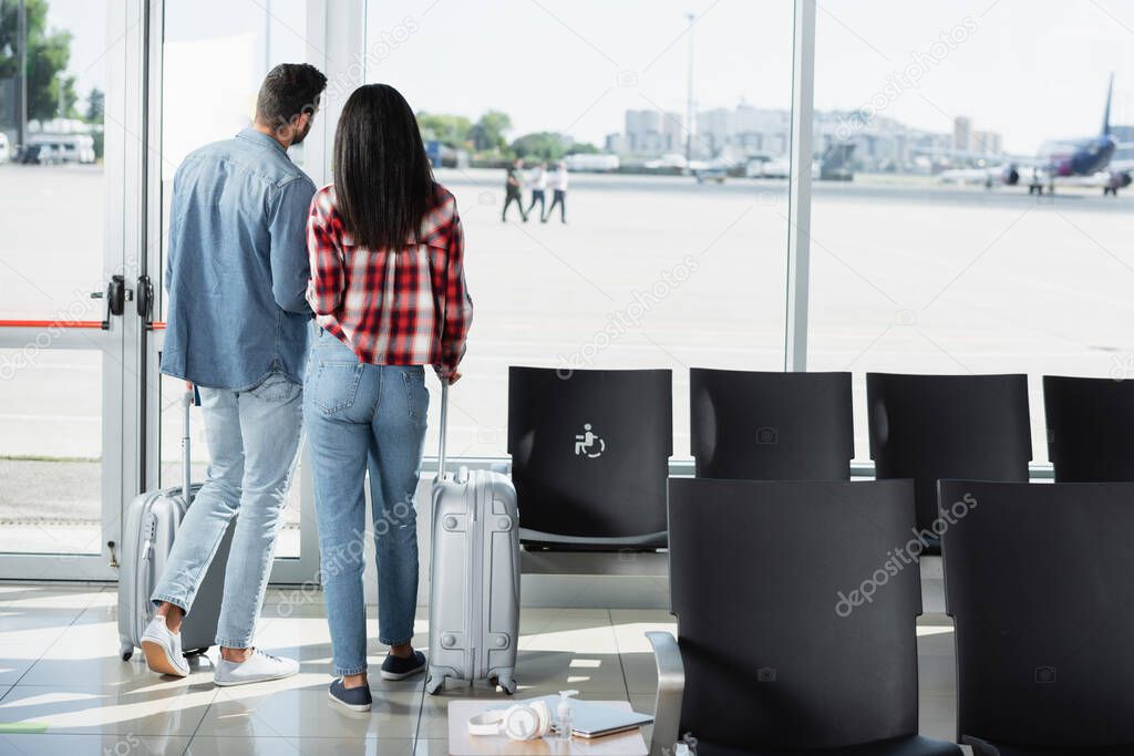 back view of couple standing with luggage in departure lounge of airport 