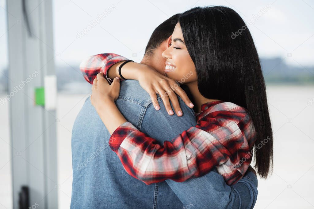 happy african american woman hugging boyfriend in airport