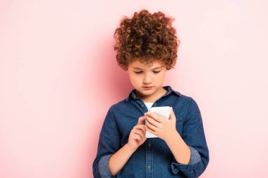 Kot gömlekli kıvırcık çocuk pembe üzerinde akıllı telefon kullanıyor.