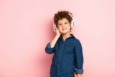 Mutlu çocuk müzik dinliyor ve pembe kulaklıklarda kablosuz kulaklıklara dokunuyor. 