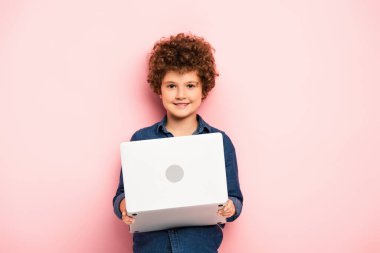 Neşeli ve kıvırcık çocuk pembe dizüstü bilgisayarı tutuyor. 