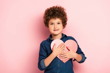 Pembe kesilmiş kalp şeklinde kağıt tutan mutlu çocuk. 