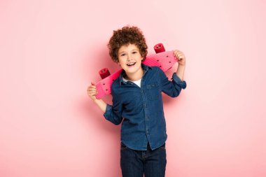 Neşeli ve kıvırcık çocuk ayakta duruyor ve pembenin üzerinde bozuk para tutuyor. 