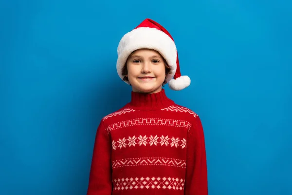 Szczęśliwy Chłopiec Kapeluszu Mikołaja Czerwony Sweter Patrząc Aparat Niebiesko — Zdjęcie stockowe