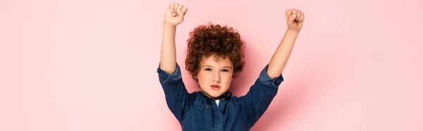 興奮した巻き毛の少年のパノラマ作物頭の上に手とピンクの上に勝者のジェスチャーを示す握りしめ拳 — ストック写真
