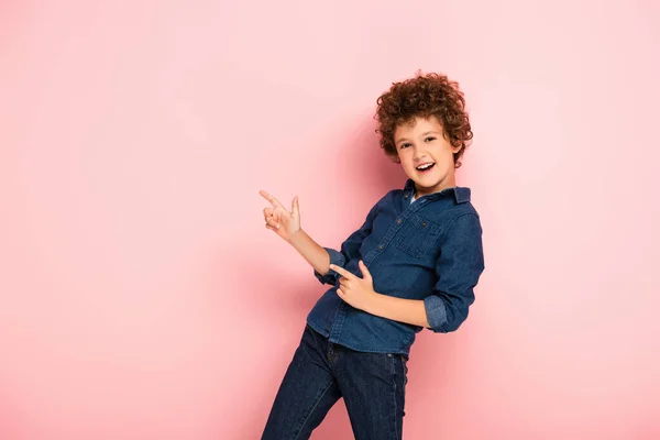 Menino Encaracolado Animado Camisa Jeans Apontando Com Dedos Rosa — Fotografia de Stock