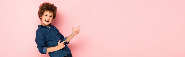 panoramic concept of excited curly boy in denim shirt pointing with fingers on pink 