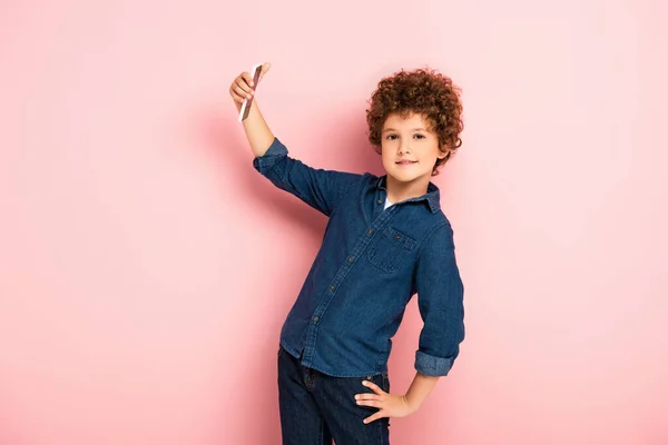 Kręcone Dziecko Dżinsowej Koszuli Robi Selfie Smartfonie Stojąc Ręką Biodrze — Zdjęcie stockowe