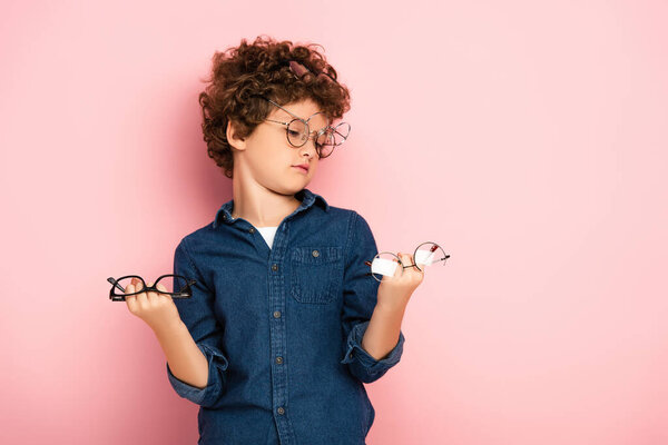 curly boy holding bunch of eyeglasses on pink  