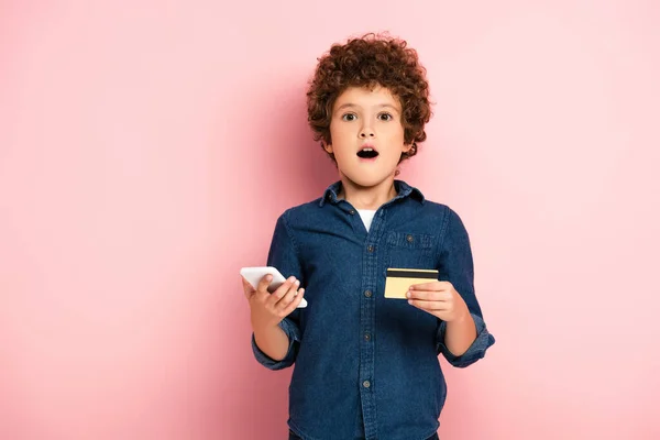 Menino Chocado Segurando Smartphone Cartão Crédito Enquanto Compras Line Rosa — Fotografia de Stock