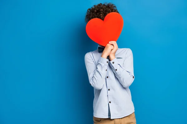 Menino Encaracolado Cobrindo Rosto Enquanto Segurando Papel Vermelho Cortar Coração — Fotografia de Stock