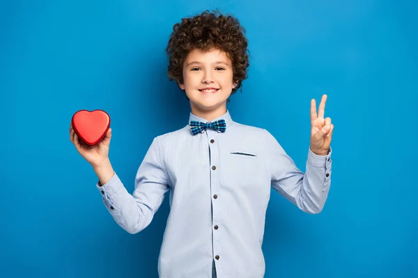 Potěšený Chlapec Drží Červené Srdce Tvaru Krabice Ukazuje Mír Znamení — Stock fotografie