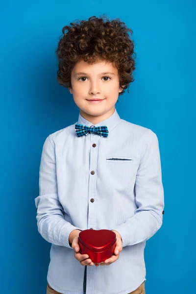 Pleased Curly Boy Holding Red Heart Shape Box Blue — Stock Photo, Image