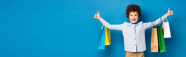 Panoramic Crop Joyful Boy Holding Shopping Bags Showing Thumbs Blue — Stock Photo, Image