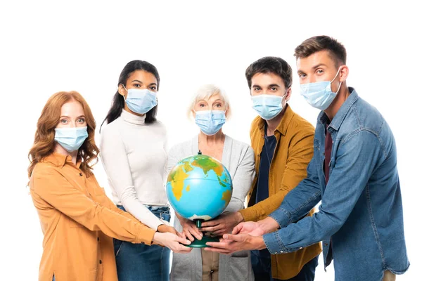 Multicultural people in medical masks looking at camera while holding globe isolated on white