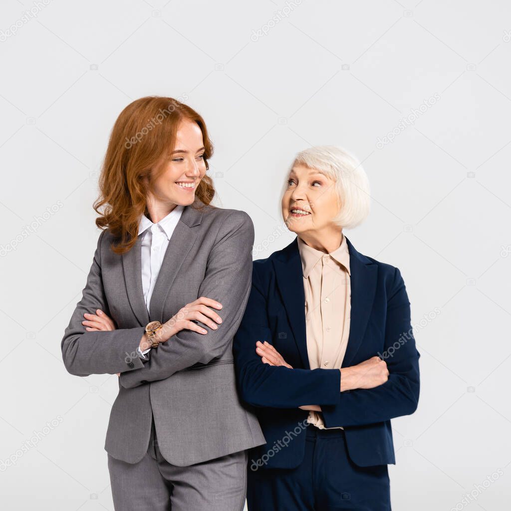 Smiling businesswomen with crossed arms looking at each other isolated on grey