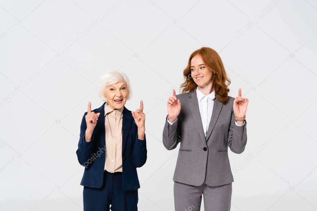 Smiling businesswomen pointing with fingers isolated on grey