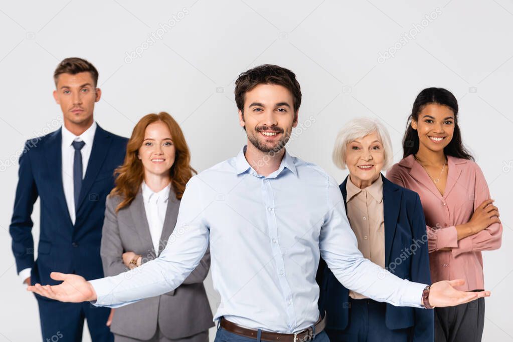 Cheerful businessman pointing with hands near multiethnic colleagues isolated on grey