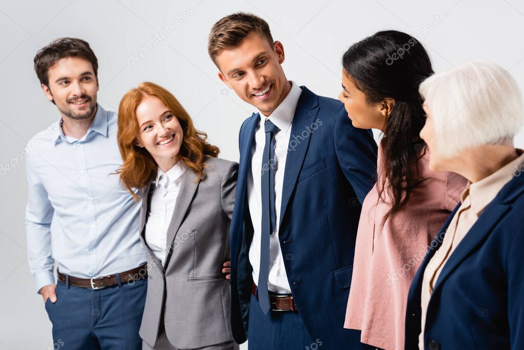 Smiling multiethnic businesspeople looking at each other isolated on grey