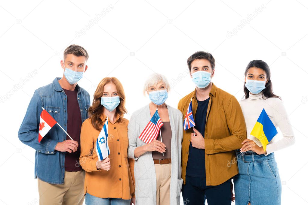 Multicultural people in medical masks holding flags and looking at camera isolated on white