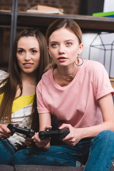 Молодые привлекательные подруги с джойстиками в руках, играющие в видеоигры дома — стоковое фото