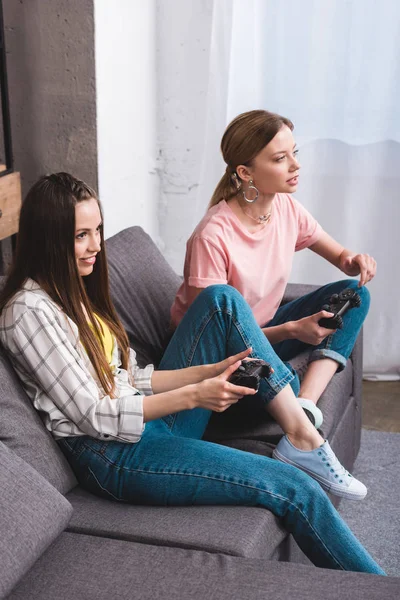 Vue grand angle de deux jeunes amies jouant à un jeu vidéo avec des joysticks dans les mains à la maison — Photo de stock
